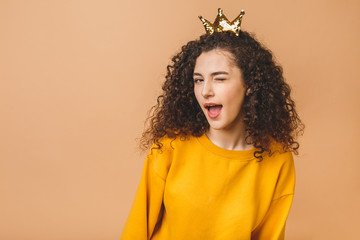 Gorgeous beautiful girl with curly brown hair and wearing casual and holding crown on head isolated...
