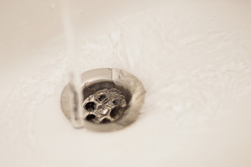 A washbasin drain with flawing water in bathroom sink