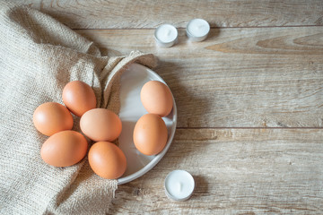 Brown eggs on a plate with textile napkin and candles on wooden rustic background. Easter composition, mockup. 