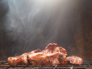 Grilled pork meat is burning on the grilling basket with tongs on the charcoal grill with white smoke causing chemicals called heterocyclic amines (HCAs), when eat is risk of produces cancer.