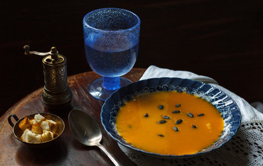 A fragment of a dining table with a plate of pumpkin soup, a vintage pepper mill and a blue glass