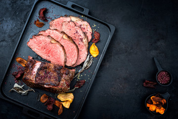 Traditional Commonwealth Sunday roast with sliced cold cuts roast beef with vegetable chips and herbs as top view on a modern design tray with copy space right