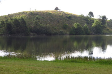 Peaceful waters of a rural dam next to a hill with late afternoon sun catching the trees