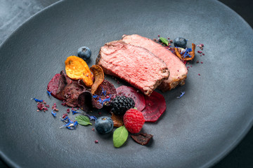 Barbecue dry aged wagyu roast beef natural sliced offered with vegetable chips and forest fruits as closeup on a modern design plate