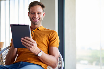 Smiling young man sitting at home using a tablet