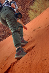 A young woman with a camera climbs a sand hill towards a mountain. Shot from the bottom. Wadi Rum desert, Jordan