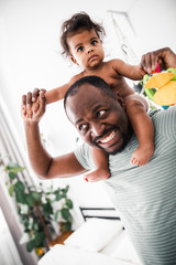Joyful Afro American man carrying baby girl on his shoulders