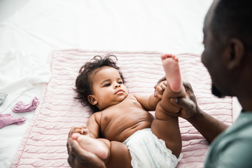 Afro American man holding legs of cute newborn daughter