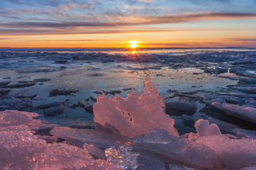 winter or spring sunset against the backdrop of a semi-frozen bay with pieces of ice and pink ice...