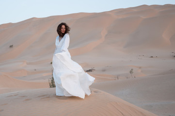 Fototapeta na wymiar Caucasian brunette woman in white dress on sand dunes in desert