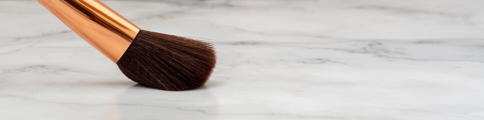 Brocha de maquillaje grande, junto a otras bochas mas pequeñas, con una espatula sobre una base de...