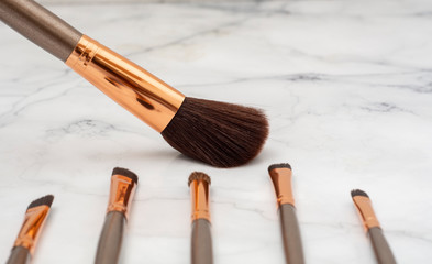 Brocha de maquillaje grande, junto a otras bochas mas pequeñas, con una espatula sobre una base de...