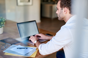 Young businessman sitting at a table at home using a laptop