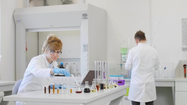 Chemist working with hemp CBD oil in laboratory and writing results in laptop.