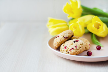 morning breakfast, oatmeal cookies with cereals and cranberries, yellow tulip flowers on white wooden background with copy space, closeup