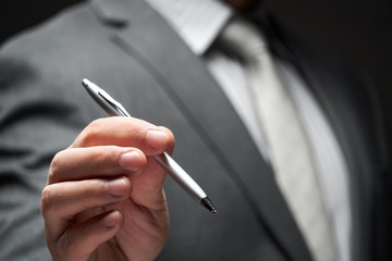 a pen closeup in businessman hand, gray suit, dark wall background