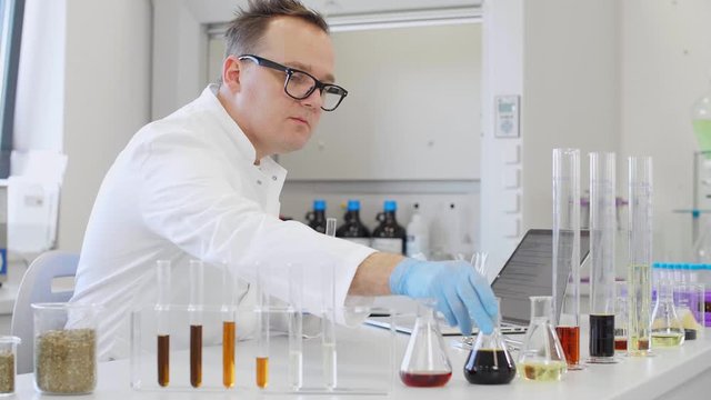 Chemist working with hemp CBD oil in laboratory and writing results in laptop.