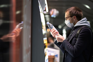 Caucasian man customer in glasses wearing facial protective mask, buying and choosing water bottle, reads information on a label. Purchase of food during the coronavirus, covid-19 epidemic in USA. 