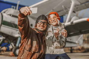 Smiling young father and son in aviator hats making selfie