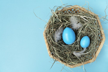 Two blue eggs in the wicker basket on the blue background. Copy space. Place for text and design. Happy Easter. Top view. Flat layout.