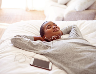 Young woman listening to music on earphones in her bed