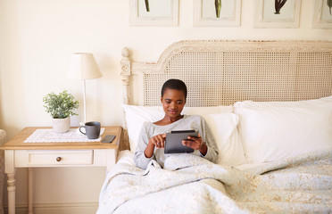 Smiling woman using a tablet in bed in the morning