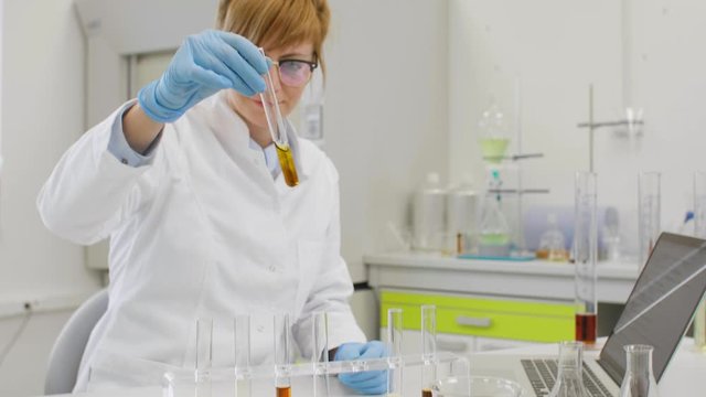 Chemist working with hemp CBD oil in laboratory and writing results in laptop.