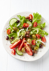 Healthy salad with various tomatoes, cucumber, olives and capers. White wooden background. Top view. 