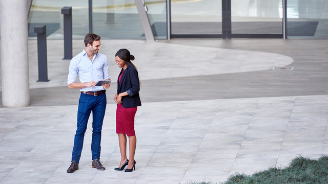 Two diverse young businesspeople smiling while talking outside their office