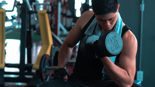 Slow motion video of Asian young muscular man lifting up weight dumbbell in gym. fitness, gym, healthy, stronger, bodybuilding, training, slow motion or indoor sport concept 