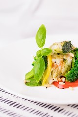 Steamed cod fish fillet with broccoli, tomato, lemon, avocado, basil sauce and pine nuts on a white background. Copy space