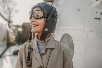 Happy little boy in aviator hat standing outdoors