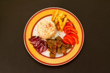 Traditional Turkish roast beef liver designed in stylish plate with fried potato,tomato,onion and rice on the black surface 