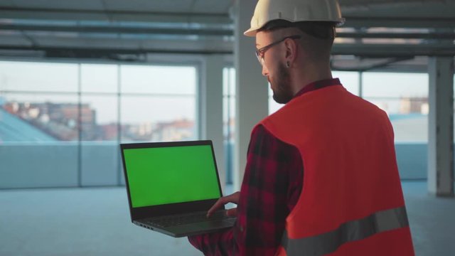Shot back man engineer using laptop computer with green screen inside building worker project occupation builder technology mock-up professional male safety device computer slow motion