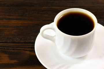 A white cup of coffee and coffee beans on a wooden table.