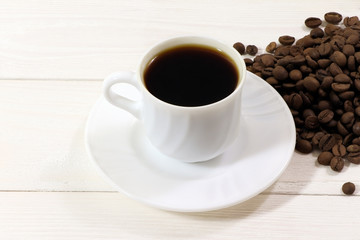 A white cup of coffee and coffee beans on a wooden table.