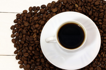 A white cup of coffee and coffee beans on a wooden table.