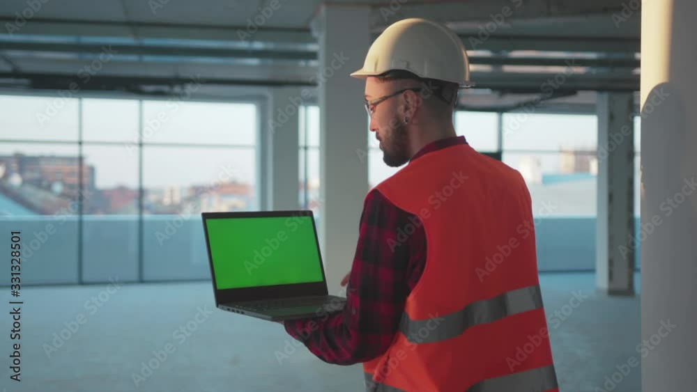 Wall mural man stand look around engineer using laptop computer with green screen inside building worker projec