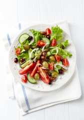 Healthy salad with various tomatoes, cucumber, olives and capers. White wooden background. Top view.