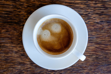White cup of fresh coffee on wooden table, top view