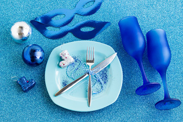 Designed Elegant Christmas Table with two blue champagne glasses,christmas ornaments,plate and two blue mask.Shiny background,top view.