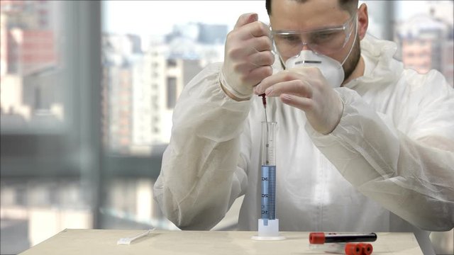 Inventing and developing medicine to fight coronavirus. Medical scientist pushing blood from syringe to the test tube with blue liquid and stirring it up to observe a reaction.