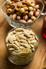 Pumpkin seeds and pistachios in glass bowls on wooden tray.Vertical image