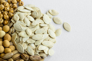 Pumpkin seeds on the white fabric surface with other nuts and copy space.