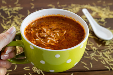 Hand holding a mug of traditional Turkish vermicelli soup on wooden background.