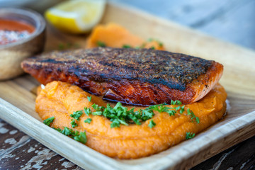 Fried salmon fillets served with vegetable garnish on wooden plate and sauce. Roasted salmon filet with sweet mashed potatoes.