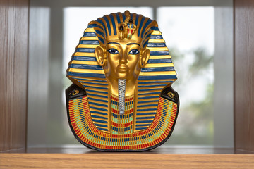 Antique Egyptian gold pharaoh Tutankhamen mask souvenir on wooden cabinet shelf for interior,...