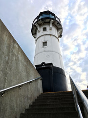 A small light house guard the entrance of a cannel that connects Lake Superior to the South Harbor of Duluth MN formed by a blue sky with clouds.