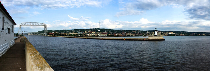 Entrance of the South Harbor of Duluth MN form Lake Superior with a simple light house on one end and a metal lift bridge on the other and the city in the background.  