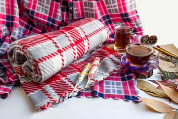 Rolled grey fleece blanket on a pink  blanket on white ground with two cups of Traditional Turkish Tea and autumn leaves.